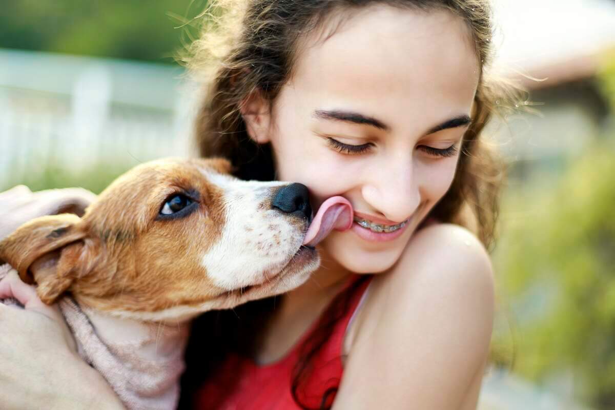 Girl being licked by tan and white puppy